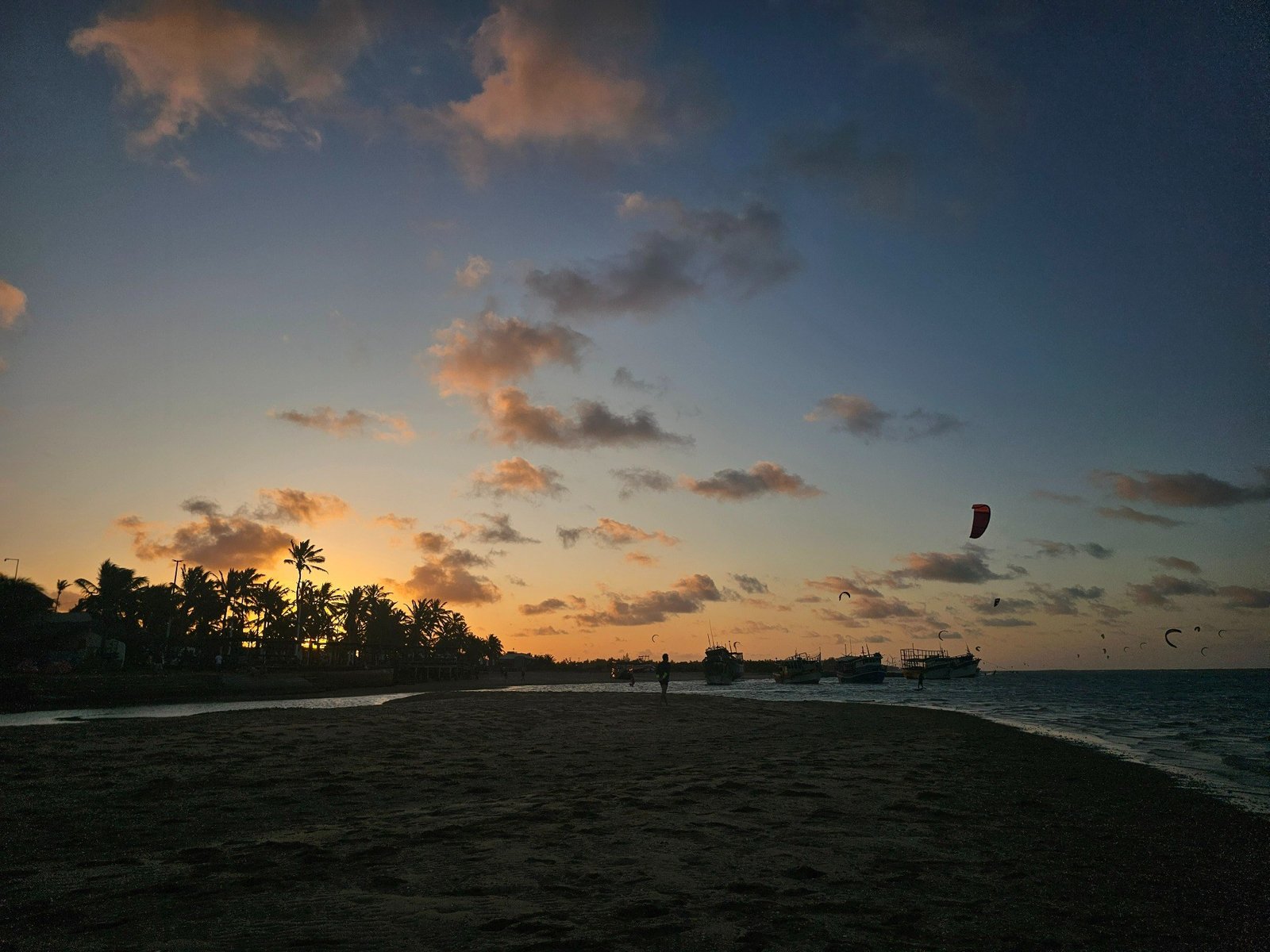 Sunset over a palm-lined Brazilian beach with kiteboarding kites above the water