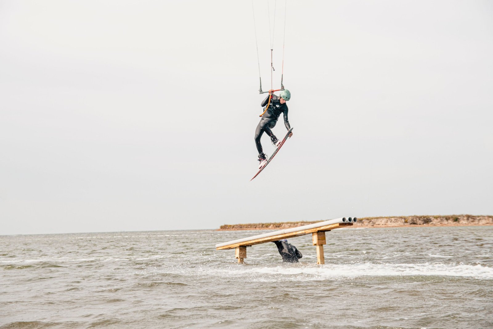 Kiteboarder jumping above a wooden rail on the water
