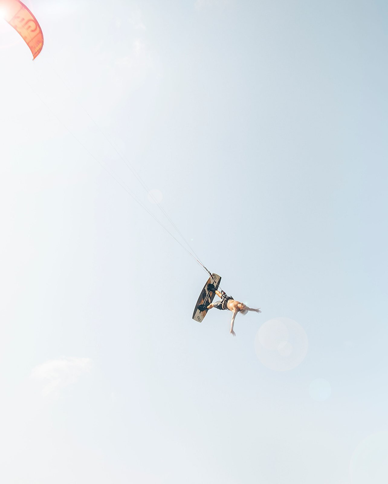 Kiteboarder performing a high aerial trick beneath an orange kite